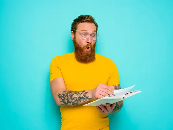 Ein Mann mit gelbem T-Shirt und Bart ist über etwas überrascht das im Buch mit lustigen Fakten steht